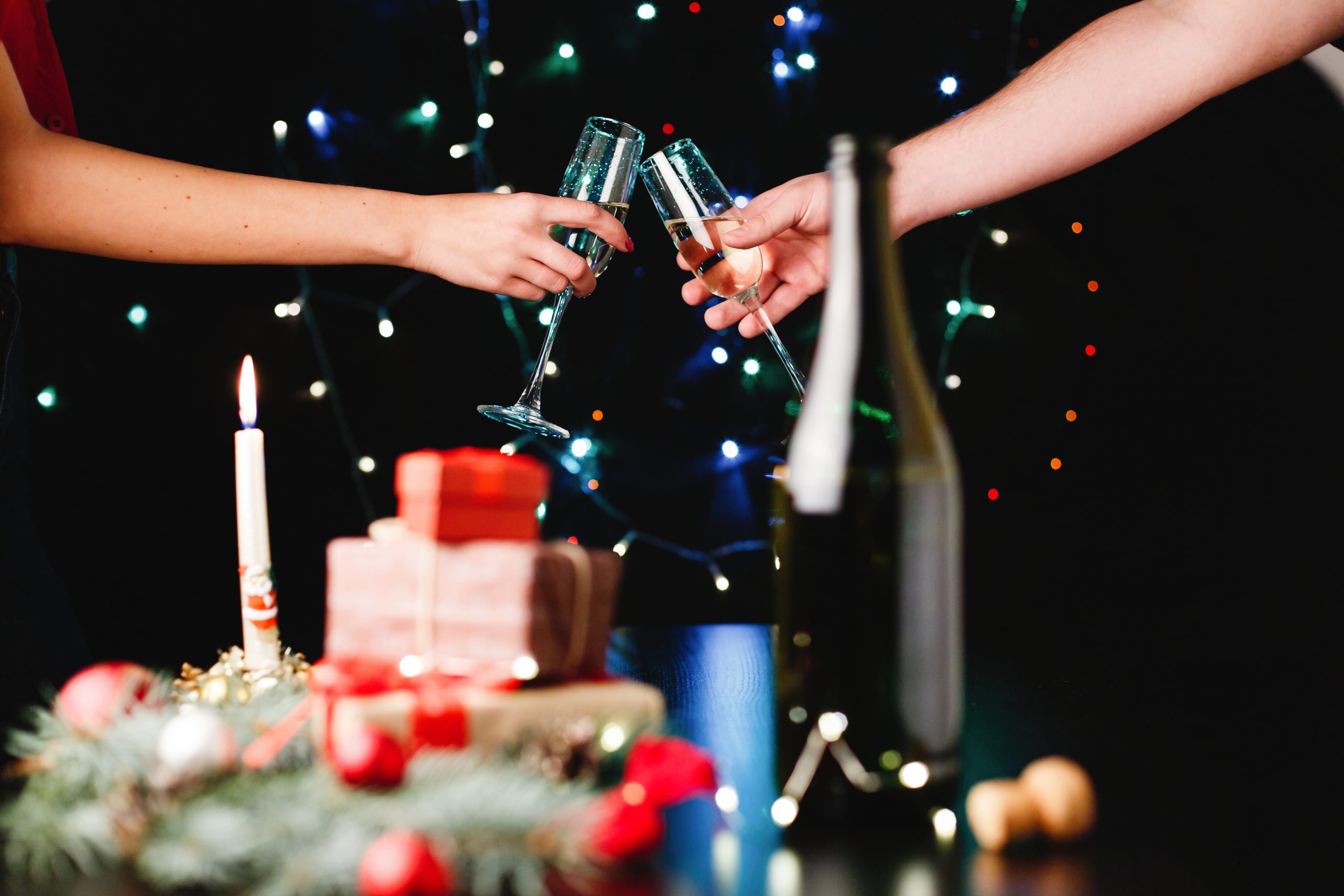 New Year and Christmas decor. People clang glasses with champagne on the background behind festive dinner table with presents